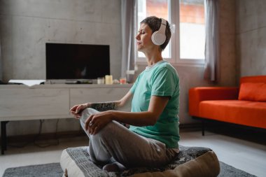 one woman senior caucasian female using headphones for online guided meditation practicing mindfulness yoga with eyes closed on the floor at home real people self care concept copy space