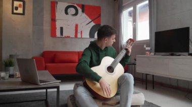 One young man Caucasian teenager sit at home in room playing guitar