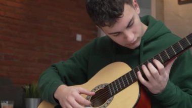 One young man Caucasian teenager sit at home in room playing guitar