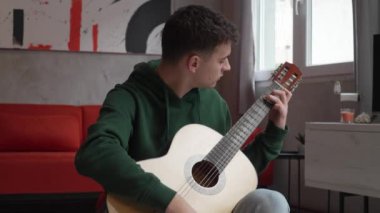 One young man Caucasian teenager sit at home in room playing guitar