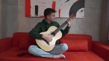 One young man Caucasian teenager sit at home in room playing guitar
