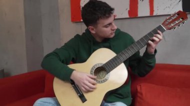 One young man Caucasian teenager sit at home in room playing guitar