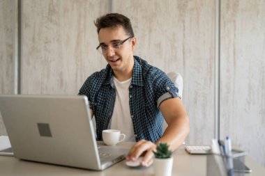 Ofiste oturan beyaz bir adam gündüz dizüstü bilgisayarda çalışıyor mavi gömlekli genç serbest işçi ya da girişimci işadamı rapor yazıyor ya da internetten iş yeri fotokopisi çekiyor.
