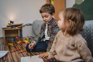 Small caucasian boy and girl siblings brother and sister children play at home draw on the floor at home childhood development growing up concept copy space domestic life