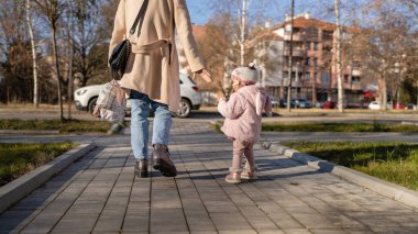 back view woman and girl mother and child go toward car in winter day