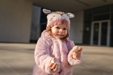 Small caucasian girl toddler play in front of building in winter day