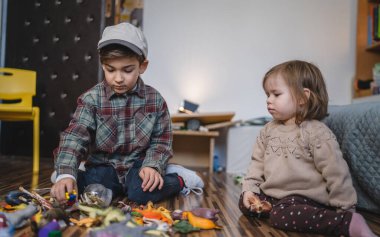 Small caucasian boy and girl siblings brother and sister children play at home sit on the floor at home childhood development growing up concept copy space domestic life