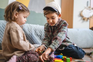 Small caucasian boy and girl siblings brother and sister children play at home sit on the floor at home childhood development growing up concept copy space domestic life