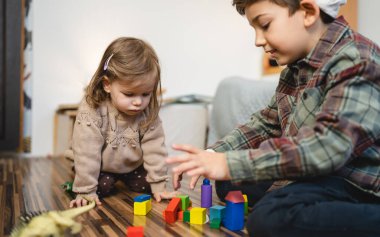Small caucasian boy and girl siblings brother and sister children play at home sit on the floor at home childhood development growing up concept copy space domestic life