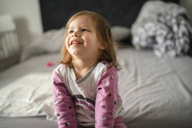 One girl small caucasian toddler sit on bed wear pajamas in morning