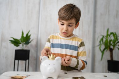 portrait of caucasian boy six years old saving money with piggy bank