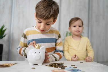 Siblings boy and girl small caucasian child brother and sister play at home with piggy bank saving money childhood investment insurance and finance concept copy space