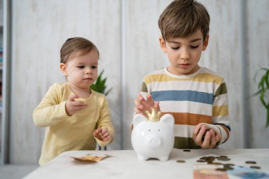 Siblings boy and girl small caucasian child brother and sister play at home with piggy bank saving money childhood investment insurance and finance concept copy space