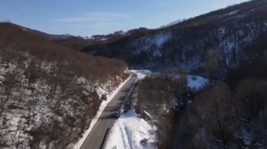 Car drive in snow winter day on the road in mountain range aerial view