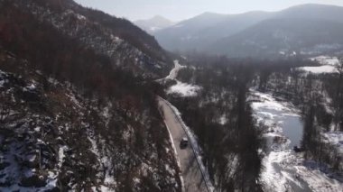 Car drive in snow winter day on the road in mountain range aerial view