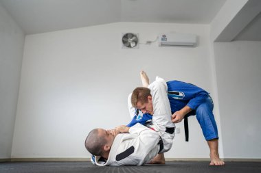 Brazilian jiu jitsu bjj training or sparing two athletes fighters dill martial arts technique at gym on the tatami mats wear kimono gi black belt instructor demonstrate submission triangle