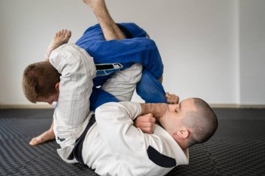 Brazilian jiu jitsu bjj training or sparing two athletes fighters dill martial arts technique at gym on the tatami mats wear kimono gi black belt instructor demonstrate submission armbar juji gatame clipart