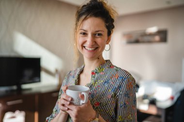 One woman happy caucasian female standing at home or hotel apartment with cup of coffee daily morning routine taking a brake real people copy space