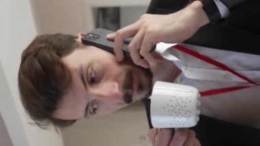 one man adult caucasian businessman wear suit in hotel room while taking a brake or prepare for work hold cup of coffee and smartphone making a phone call talk real people