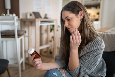 One woman young caucasian female hold medicine drugs pills tablets while siting at home smoke cigarette thinking trying to quit smoking real person copy space