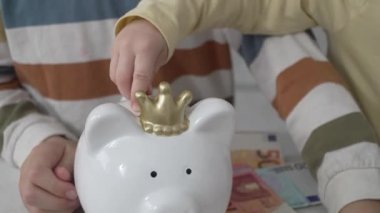 close up on hands of unknown children putting money coins in the piggy bank finance and saving investment concept