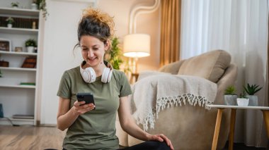 One woman sit on the floor at home with headphones use smart-phone for music listening or search for podcast online meditation or audiobook on her smarphone mobile phone online on internet copy space