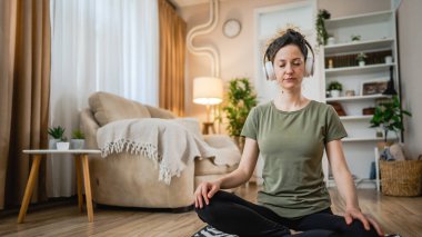 one woman adult caucasian female millennial using headphones for online guided meditation practicing mindfulness yoga with eyes closed sit on the floor at home real people self care concept copy space