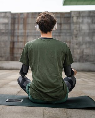 Genç, yetişkin, beyaz bir erkek, yoga ya da meditasyon için kapalı. Kulaklıkla dışarıda otururken iç huzuru ve denge kavramını gerçek insanlara uyguluyor.
