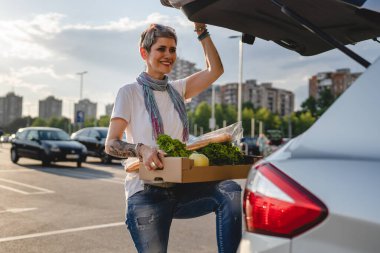 Yetişkin bir kadın, alışveriş merkezinin otoparkında arabasının bagajında duran beyaz bir kadın ya da sebzeli sebzeli bir market.