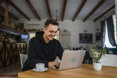 Kafe restoranının masasında oturan beyaz bir erkek siyah kapüşonlu giyiyordu. Bilgisayarla interneti tarıyor ya da serbest çalışıyordu. Uzaktan kumandalı insanlar uzay gülüşünü başarıyla taklit ediyordu.