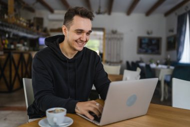 Kafe restoranının masasında oturan beyaz bir erkek siyah kapüşonlu giyiyordu. Bilgisayarla interneti tarıyor ya da serbest çalışıyordu. Uzaktan kumandalı insanlar uzay gülüşünü başarıyla taklit ediyordu.