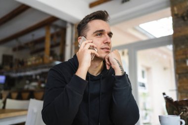 One man sitting at the table at cafe or restaurant wear casual using mobile phone to make a call talking communication while hold a cup of coffee real people copy space serious