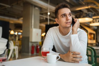 Genç yetişkin bir erkek kafeteryada ya da restoranda cep telefonuyla konuşuyor gerçek insanlar uzayı kopyalıyor.