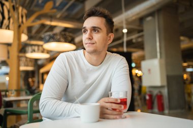 Kafeteryada ya da restoranda tek başına oturan, meyveli su içen, genç, yetişkin bir erkek. Gerçek insanlar gülümser.