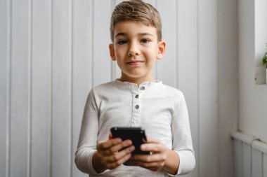 one boy caucasian child preschooler hold smartphone mobile phone at home play video games childhood and growing up technology addiction concept use smartphone app for online browsing or watch video