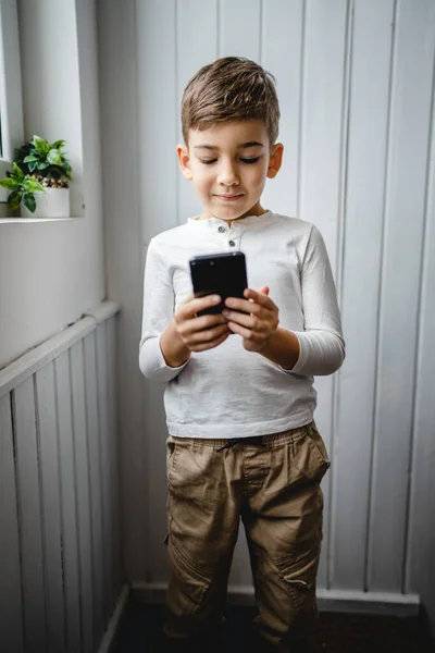 stock image one boy caucasian child preschooler hold smartphone mobile phone at home play video games childhood and growing up technology addiction concept use smartphone app for online browsing or watch video