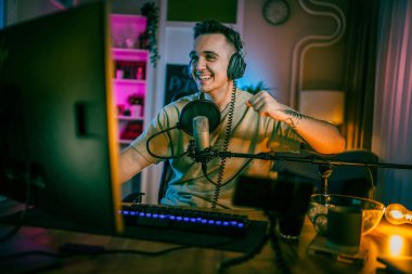 Young man play video games on pc computer while streaming to social media or internet online playtrough or walktrough video male gamer having fun at home wear headphone happy winning copy space