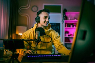Young man play video games on pc computer while streaming to social media or internet online playtrough or walktrough video male gamer having fun at home wear headphone copy space