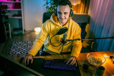 Young man play video games on pc computer while streaming to social media or internet online playtrough or walktrough video male gamer having fun at home wear headphone copy space