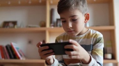 Kafkasyalı bir çocuk anaokulu öğrencisi akıllı cep telefonunu evde tutuyor video oyunları oynuyor ve büyüyen teknoloji bağımlılığı kavramını kullanıyor çevrimiçi tarama veya video izlemek için uygulama kullanıyor