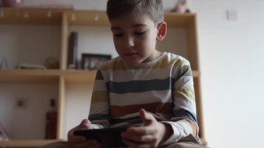 Kafkasyalı bir çocuk anaokulu öğrencisi akıllı cep telefonunu evde tutuyor video oyunları oynuyor ve büyüyen teknoloji bağımlılığı kavramını kullanıyor çevrimiçi tarama veya video izlemek için uygulama kullanıyor