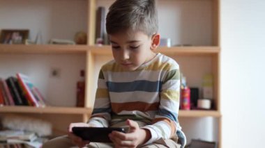 Kafkasyalı bir çocuk anaokulu öğrencisi akıllı cep telefonunu evde tutuyor video oyunları oynuyor ve büyüyen teknoloji bağımlılığı kavramını kullanıyor çevrimiçi tarama veya video izlemek için uygulama kullanıyor