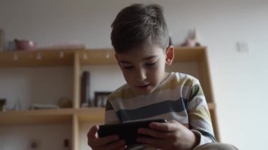 Kafkasyalı bir çocuk anaokulu öğrencisi akıllı cep telefonunu evde tutuyor video oyunları oynuyor ve büyüyen teknoloji bağımlılığı kavramını kullanıyor çevrimiçi tarama veya video izlemek için uygulama kullanıyor