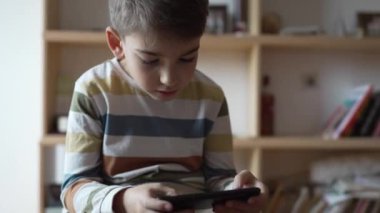 Kafkasyalı bir çocuk anaokulu öğrencisi akıllı cep telefonunu evde tutuyor video oyunları oynuyor ve büyüyen teknoloji bağımlılığı kavramını kullanıyor çevrimiçi tarama veya video izlemek için uygulama kullanıyor