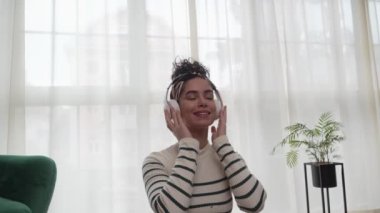 Yetişkin bir kadın Kafkas kadın nesli Z kulaklıkları internet rehberli meditasyon için kullanıyor. Düşünce yogası yapıyor, gözleri kapalı evde oturuyor. Gerçek insanlar kendi başının çaresine bakıyor.
