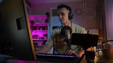 Genç adam sosyal medyaya ya da internete çevrimiçi oyun parkına bağlanırken bilgisayar oyunu oynuyor ya da evde eğlenen erkek oyuncu kulaklık takıyor ve kulaklık takıyor.