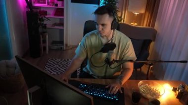 Genç adam sosyal medyaya ya da internete çevrimiçi oyun parkına bağlanırken bilgisayar oyunu oynuyor ya da evde eğlenen erkek oyuncu kulaklık takıyor ve kulaklık takıyor.