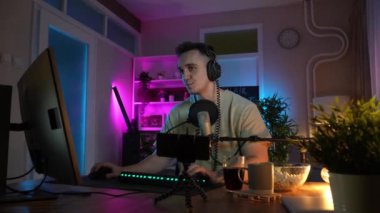 Genç adam sosyal medyaya ya da internete çevrimiçi oyun parkına bağlanırken bilgisayar oyunu oynuyor ya da evde eğlenen erkek oyuncu kulaklık takıyor ve kulaklık takıyor.