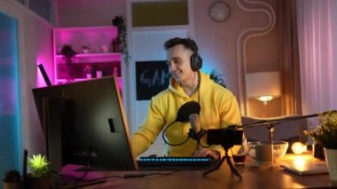 Genç adam sosyal medyaya ya da internete çevrimiçi oyun parkına bağlanırken bilgisayar oyunu oynuyor ya da evde eğlenen erkek oyuncu kulaklık takıyor ve kulaklık takıyor.