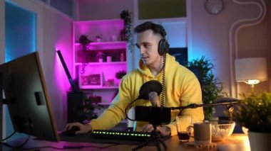 Genç adam sosyal medyaya ya da internete çevrimiçi oyun parkına bağlanırken bilgisayar oyunu oynuyor ya da evde eğlenen erkek oyuncu kulaklık takıyor ve kulaklık takıyor.
